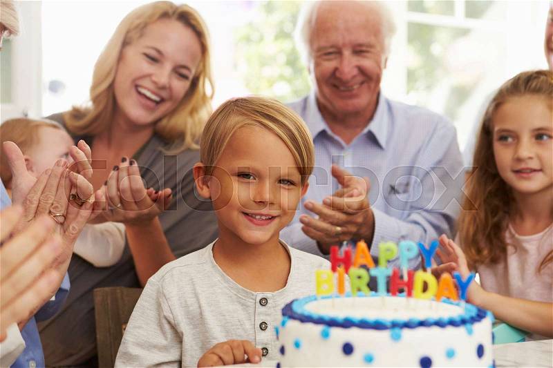 Boy Blows Out Birthday Cake Candles At Family Party, stock photo