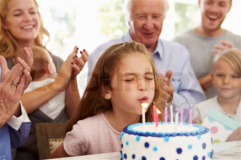 Girl Blows Out Birthday Cake Candles At Family Party, stock photo