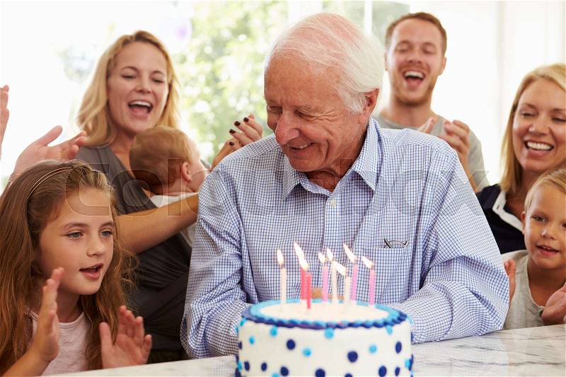 Grandfather Blows Out Birthday Cake Candles At Family Party, stock photo