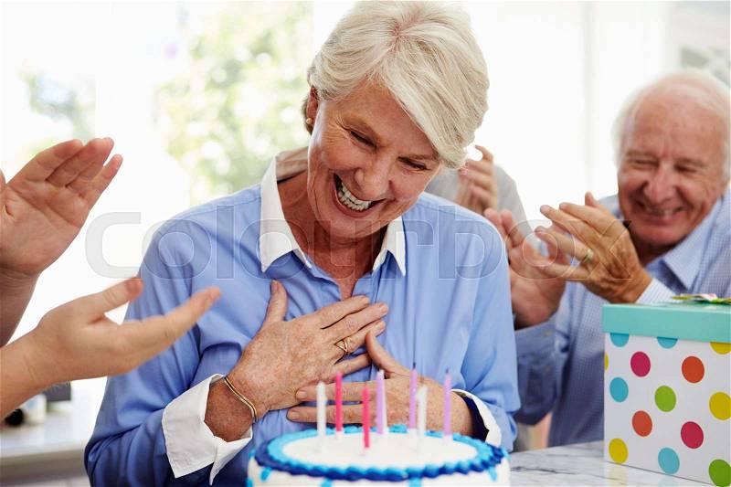 Senior Woman Blows Out Birthday Cake Candles At Family Party, stock photo