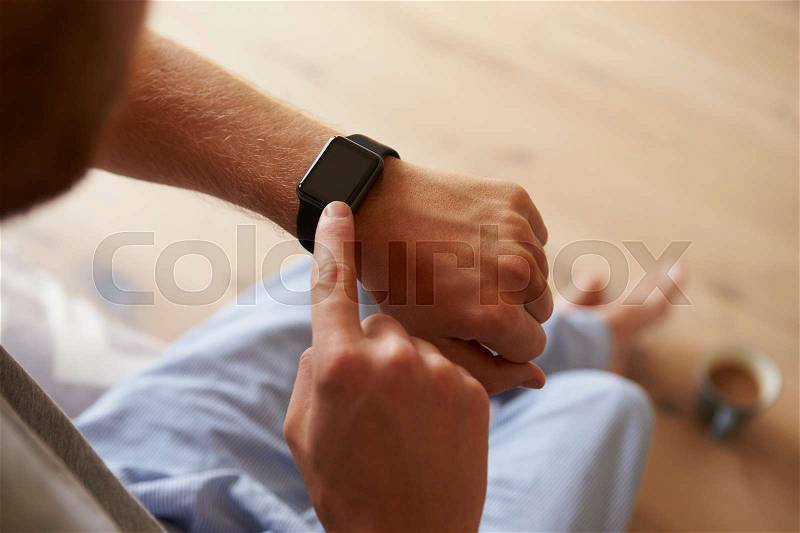 Man Wearing Pajamas Checking Smart Watch In Bedroom, stock photo