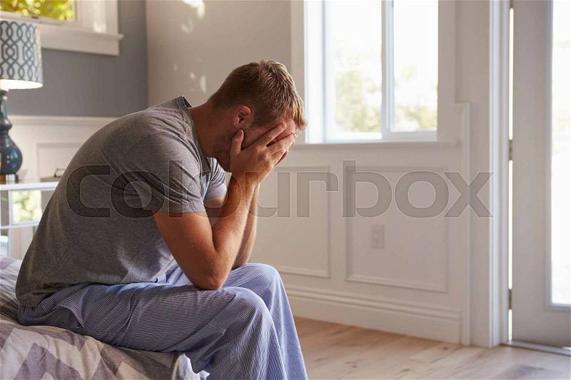 Man Wearing Pajamas Sitting On Bed With Head In Hands, stock photo