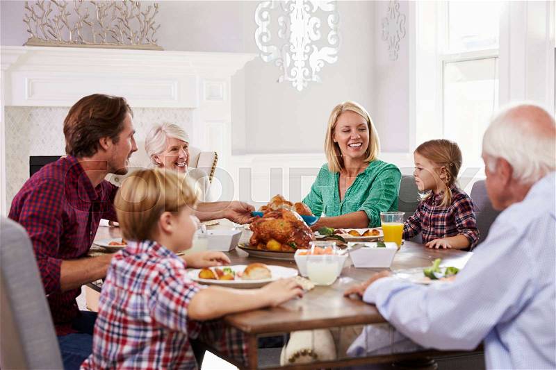 Extended Family Group Sit Around Table Eating Meal At Home, stock photo