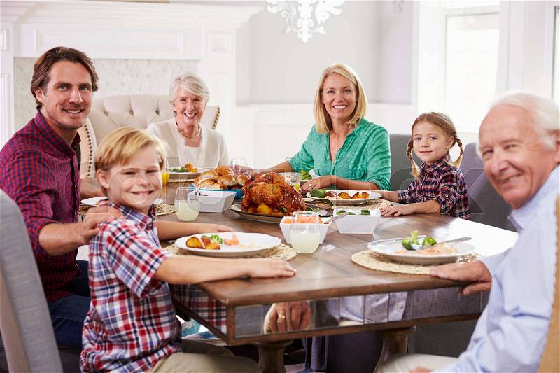Extended Family Group Sit Around Table Eating Meal At Home, stock photo