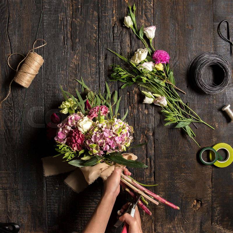 The hands of florist against desktop with working tools and ribbons on wooden background, stock photo