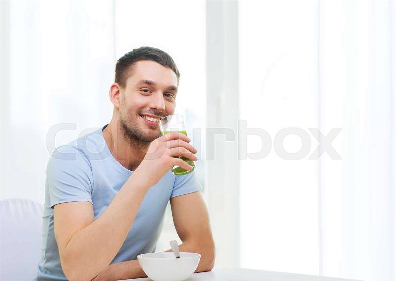 Healthy lifestyle concept - smiling happy man having breakfast at home and drinking green juice or smoothie, stock photo