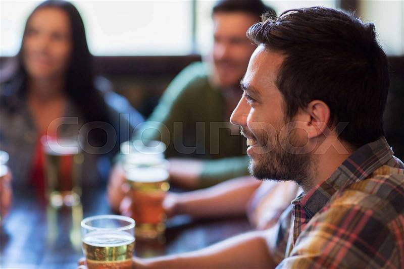 People, leisure, friendship and communication concept - happy man with friends drinking beer at bar or pub, stock photo