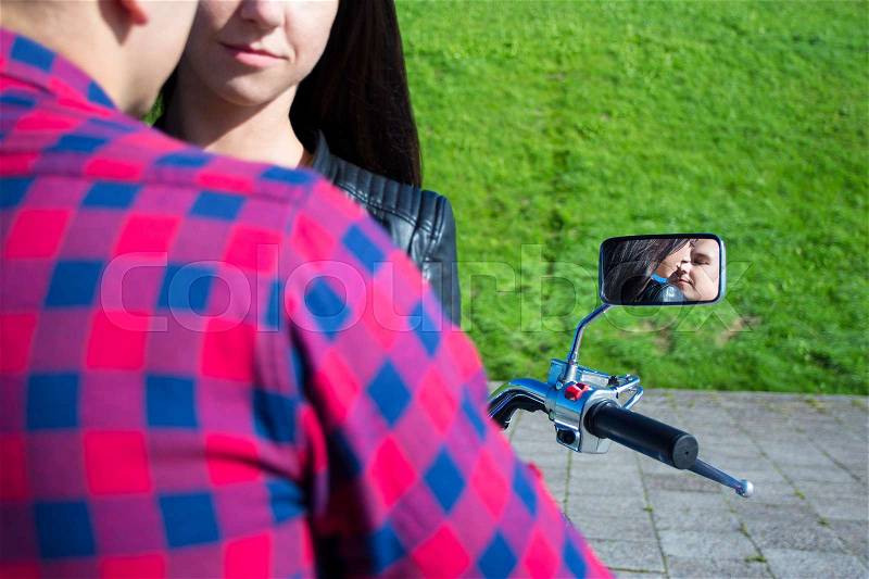 Reflection of young kissing couple in motorbike mirror, stock photo