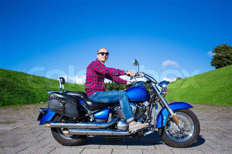 Young handsome man sitting on blue retro motorcycle, stock photo