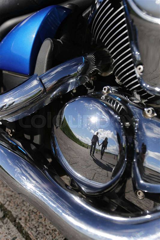 Reflection of young couple in retro motorbike motor, stock photo