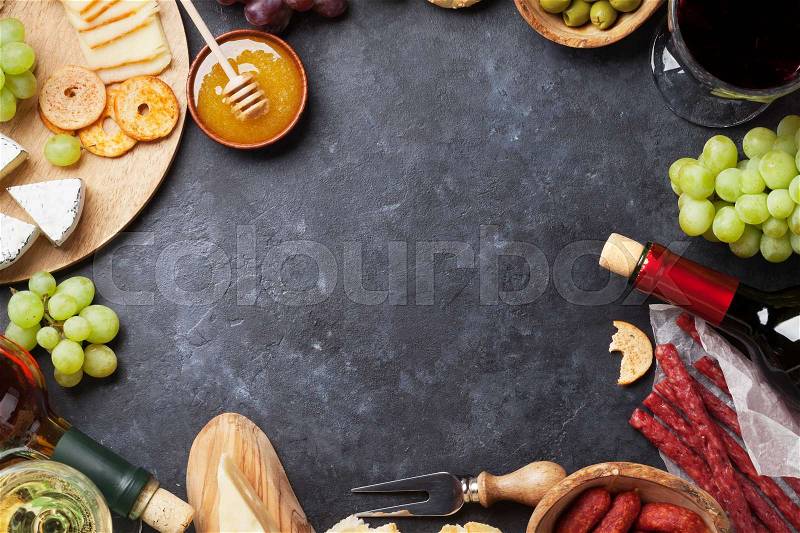 Red and white wine, grape, cheese and sausages over stone table. Top view with copy space, stock photo