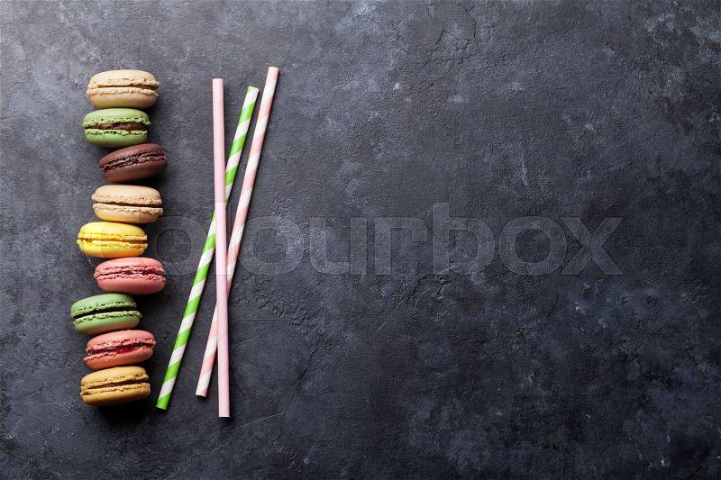 Colorful macaroons and drinking straws on stone table. Sweet macarons. Top view with copy space for your text, stock photo