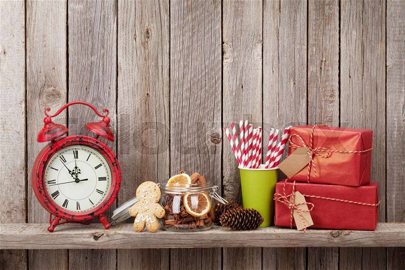 Christmas gift boxes, alarm clock and food decor in front of wooden wall. View with copy space, stock photo