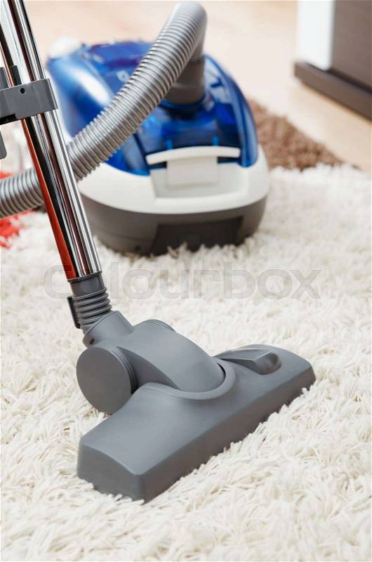Blue vacuum cleaner on shaggy carpet inside room close up, stock photo