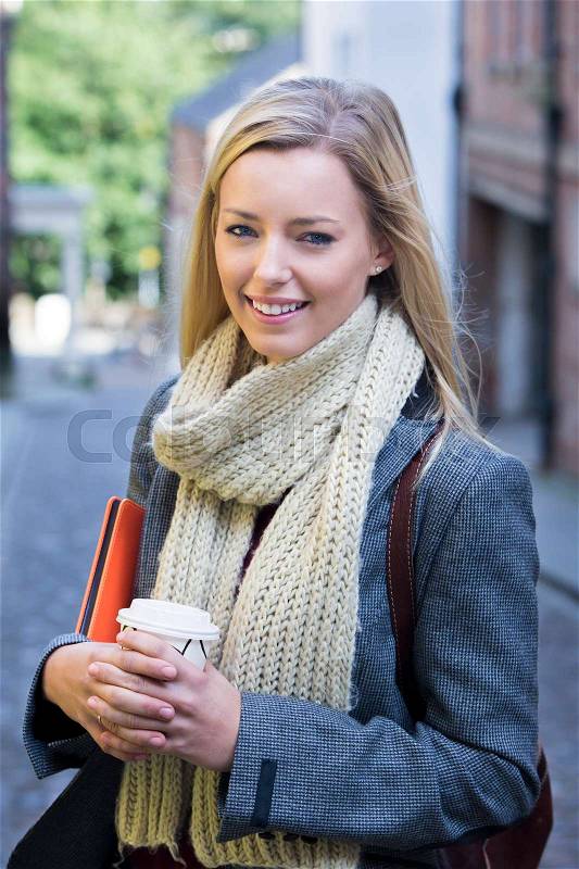 A happy female student smiles at the camera as she stands in a cobbled street on a break from studying, stock photo