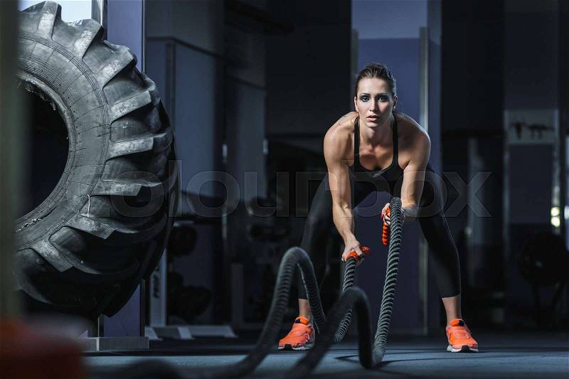 Concept: power, strength, healthy lifestyle, sport. Powerful attractive muscular woman CrossFit trainer do battle workout with ropes at the gym, stock photo