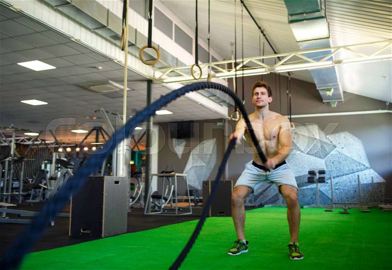 Athletic man with battle rope in functional training fitness gym, stock photo