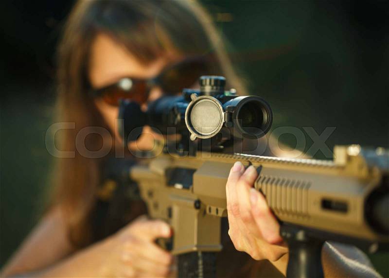 A young girl with a gun for trap shooting and shooting glasses aiming at a target, stock photo