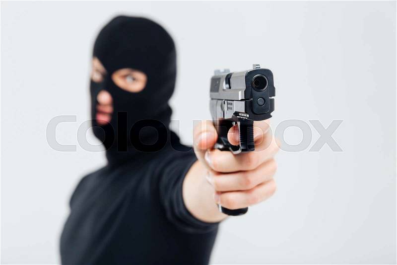 Man robber in balaclava pointing with gun, stock photo