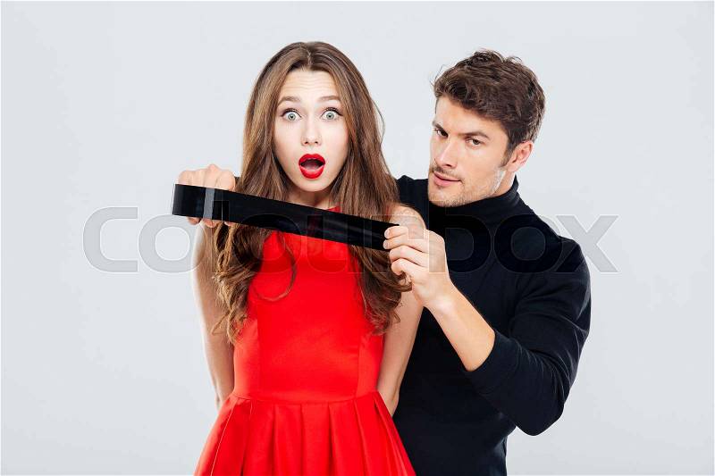 Cryminal man covering mouth of scared young woman with tape, stock photo