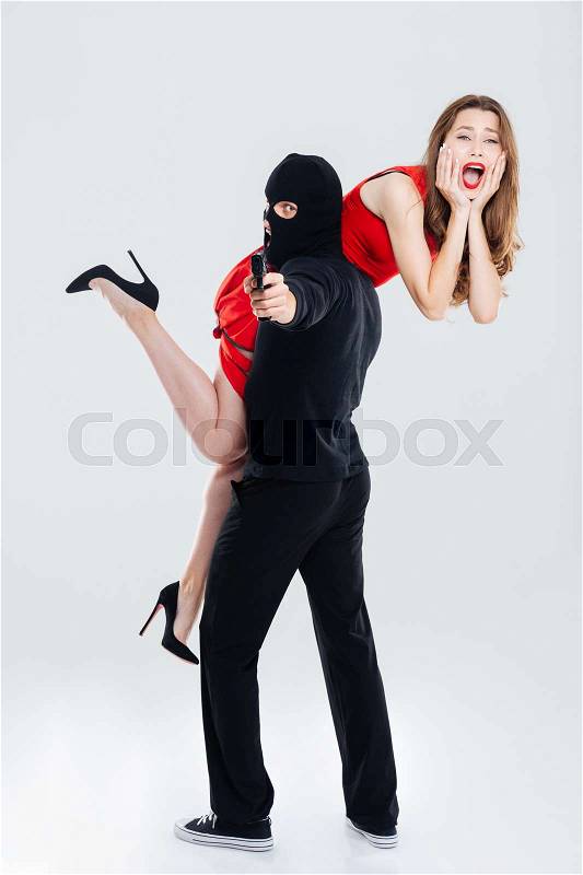 Man in balaclava stealing young woman and pointing gun on you, stock photo