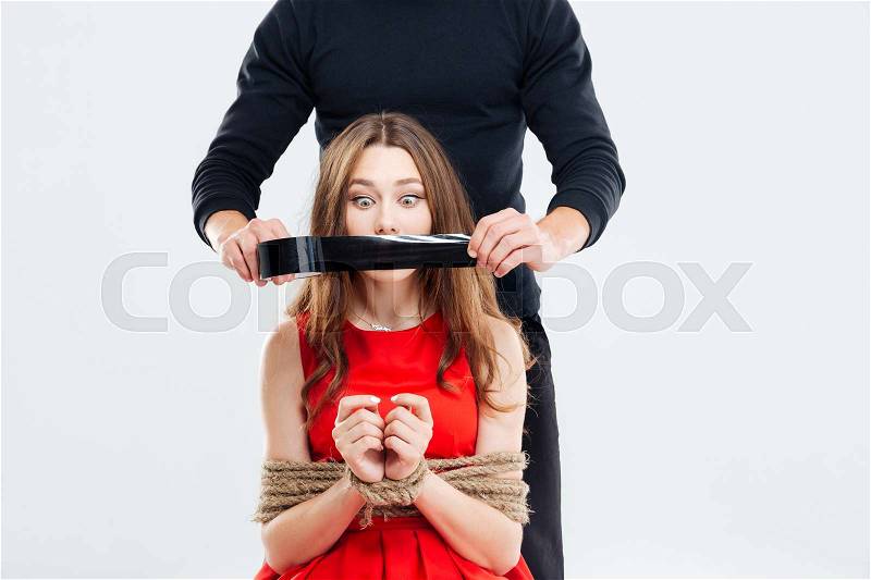 Criminal man covering mouth of woman bounded with ropes by black tape, stock photo