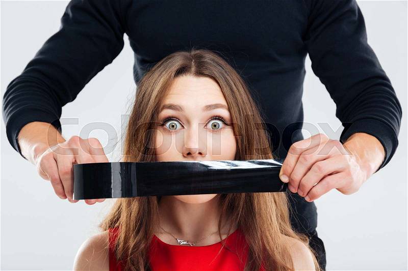 Closeup of man covering mouth of woman by black tape, stock photo