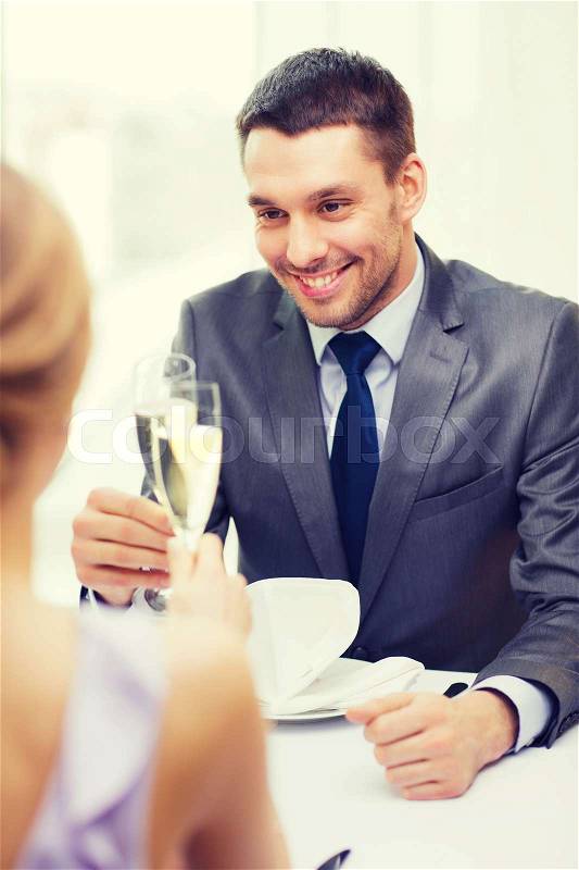 Restaurant, couple and holiday concept - smiling man with glass of champagne looking at wife or girlfriend at restaurant, stock photo