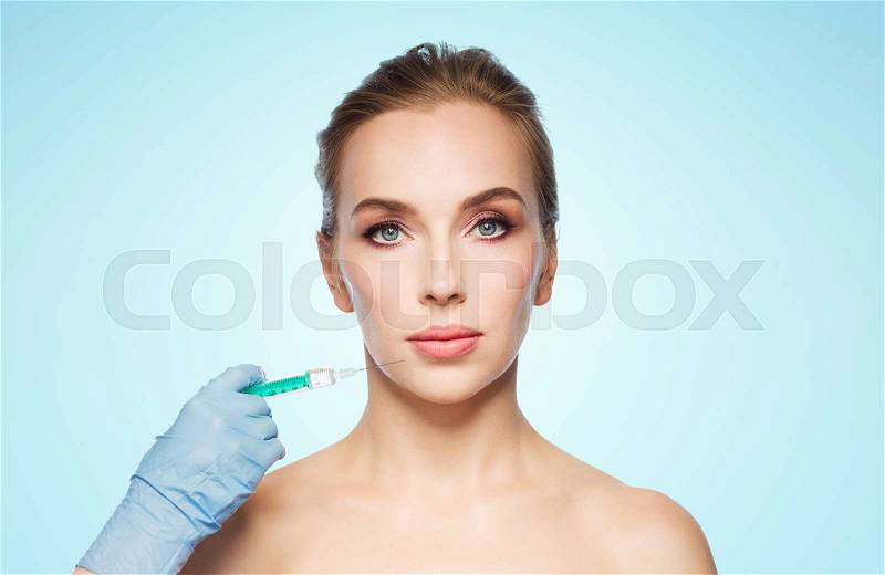 People, cosmetology, plastic surgery and beauty concept - beautiful young woman face and beautician hand in glove with syringe making injection over blue background, stock photo