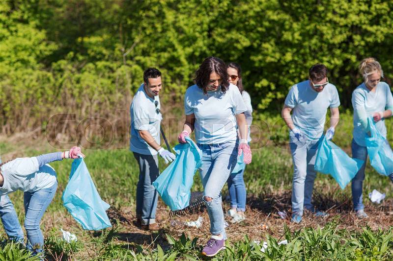 Volunteering, charity, cleaning, people and ecology concept - group of happy volunteers with garbage bags cleaning area in park, stock photo