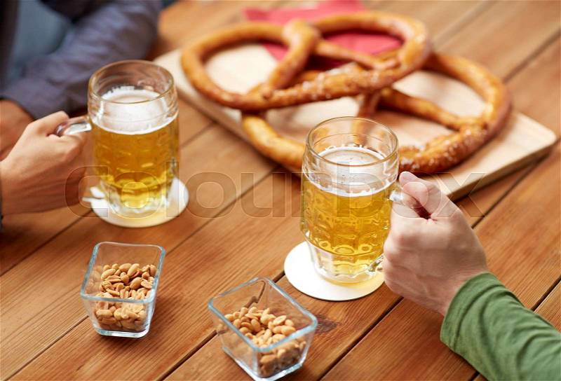 People, leisure and drinks concept - close up of male hands with beer mugs and pretzels at bar or pub, stock photo