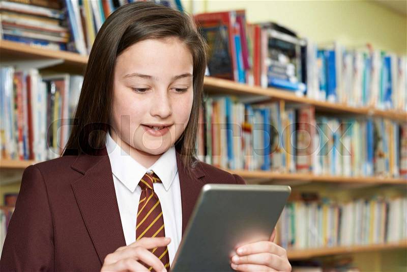 Girl Wearing School Uniform Using Digital Tablet In Library, stock photo