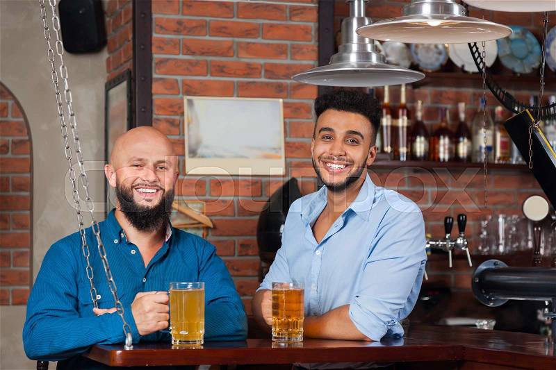 Two Mix Race Man In Bar Hold Glasses Sit At Counter, Drinking Beer, Cheerful Friends Meeting Pub Communicate Talking, stock photo