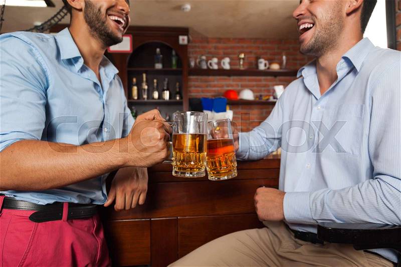 Two Man In Bar Clink Glasses Toasting Sit At Table, Drinking Beer Hold Mugs Close Up, Friends Wear Shirts Pub Communicate Talking, stock photo