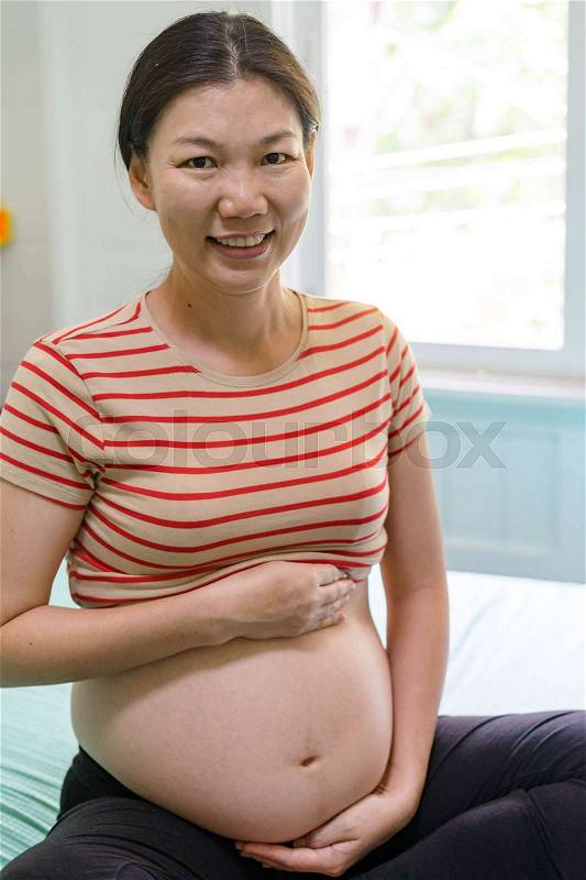 Happy pregnant woman sitting in home, stock photo