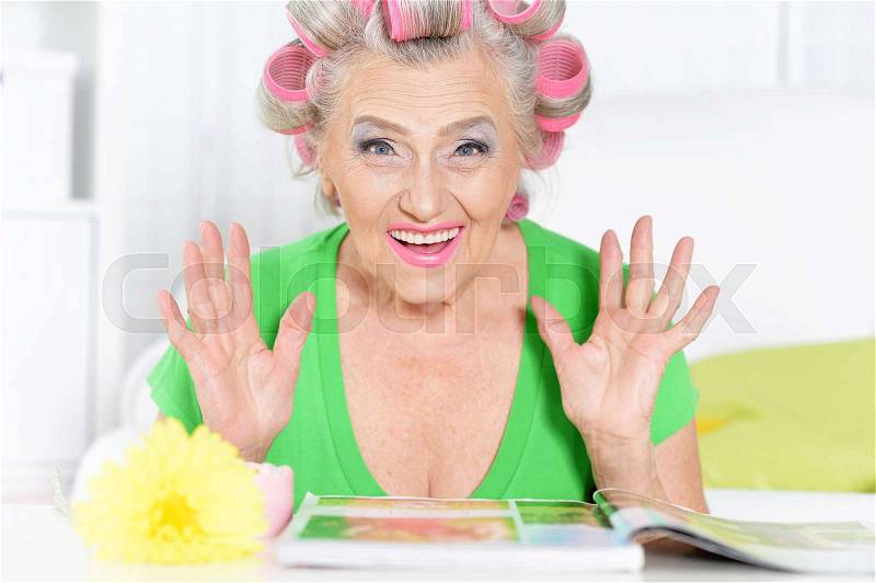 Senior woman in hair rollers with magazine at home, stock photo