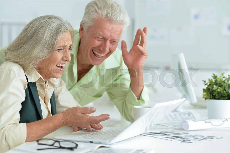 Happy senior couple with laptop in office, stock photo