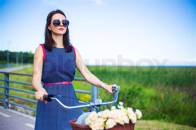 Portrait of happy young woman riding on bicycle with wicker basket, stock photo