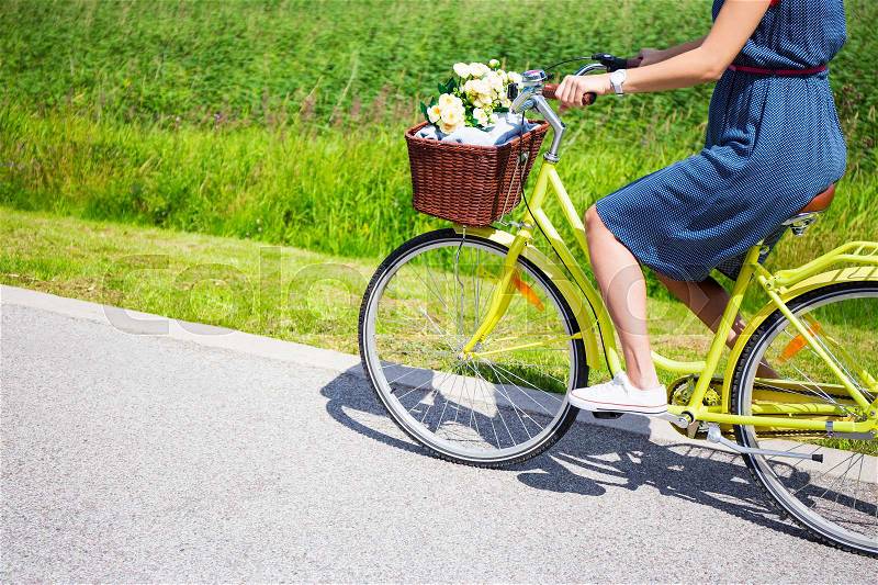 Woman riding vintage bicycle with wicker basket and flowers, stock photo