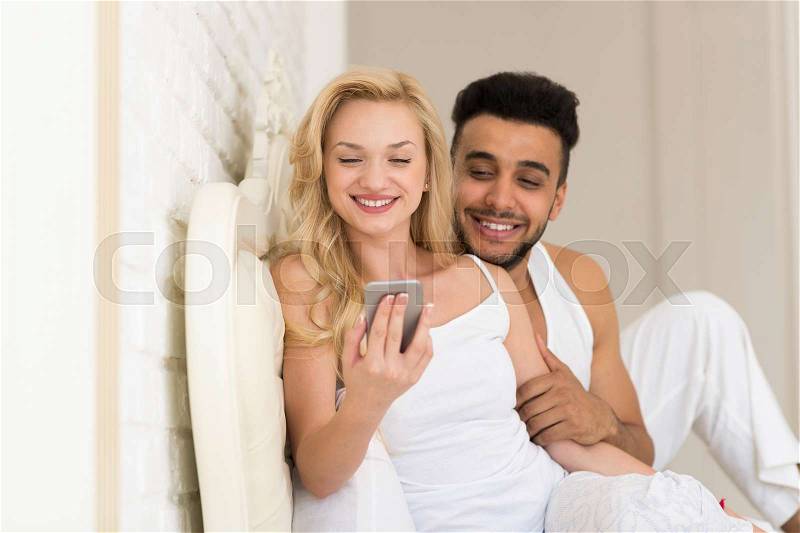 Young Couple Lying In Bed, Happy Smile Hispanic Man And Woman Using Cell Smart Phone, Lovers In Bedroom, stock photo