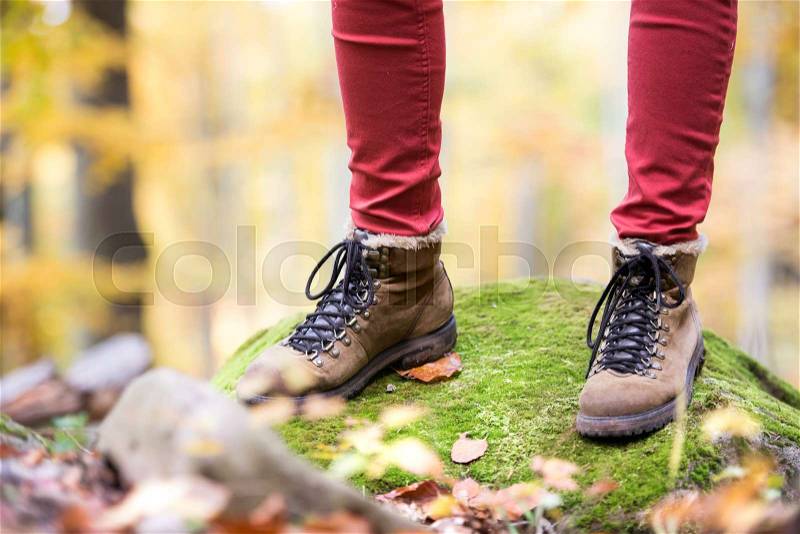 Close up of legs of unrecognizable woman in autumn nature standing on a rock covered with green moss. Hiking shoes, stock photo