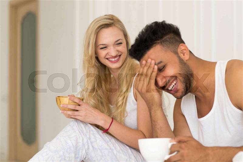 Young Couple Drink Coffee Sitting In Bed Laughing, Happy Smile Young Hispanic Man And Woman Lovers Hold Cups Bedroom, stock photo