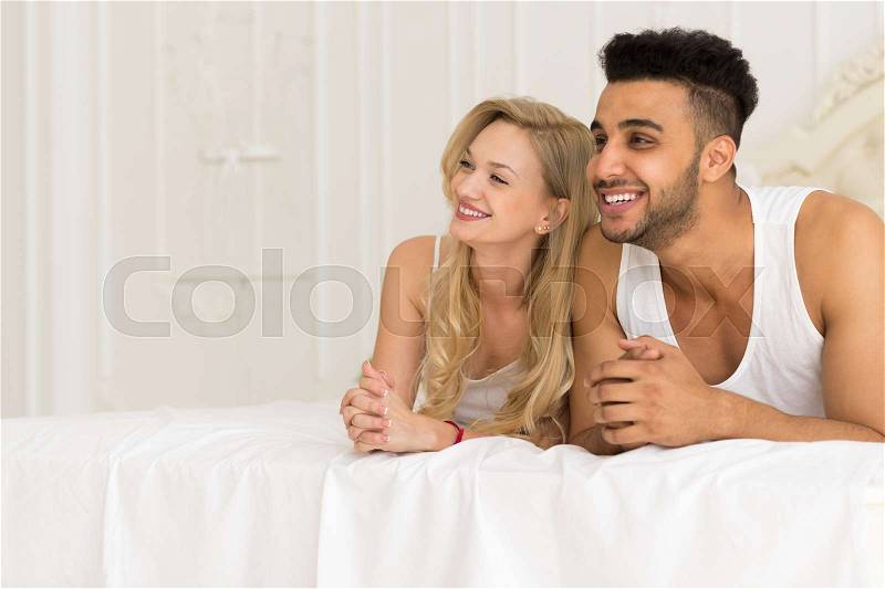 Young Couple Lying In Bed, Happy Smile Hispanic Man And Woman Lovers In Bedroom Looking Up To Copy Space, stock photo