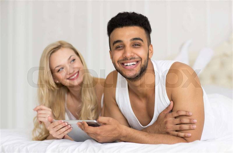 Young Couple Lying In Bed, Happy Smile Hispanic Man And Woman Using Tablet Computer, Lovers In Bedroom, stock photo