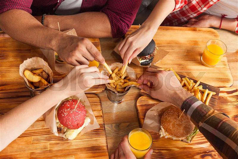 People Group Friends Hands Eating Fast Food Burgers Potato Drinking Orange Juice, Cafe Wooden Table Top Angle View, stock photo