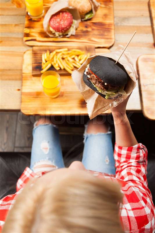 Beautiful Blonde Woman Eat Beef Burger Top Angle View, Young Girl Sitting In Fast Food Cafe, stock photo