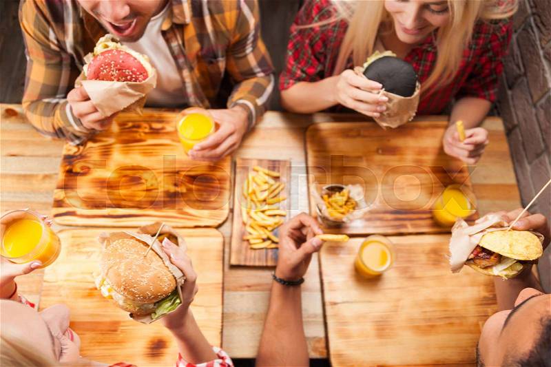 People Group Friends Eating Fast Food Burgers Potato Drinking Orange Juice, Cafe Wooden Table Top Angle View, stock photo