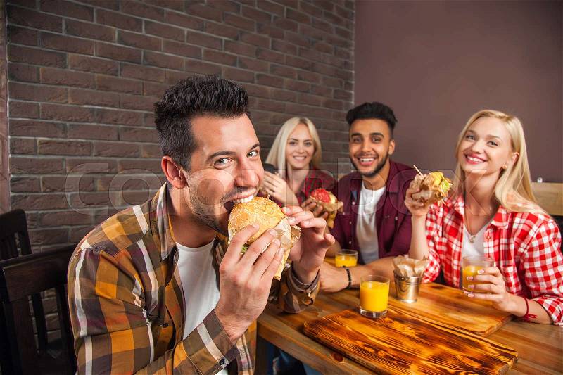 People Group Eating Fast Food Burgers Sitting At Wooden Table In Cafe, Friends Meeting Communication, stock photo