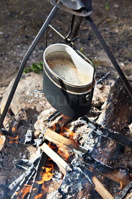 Food is prepared into pot over campfire in hike on fishing, stock photo