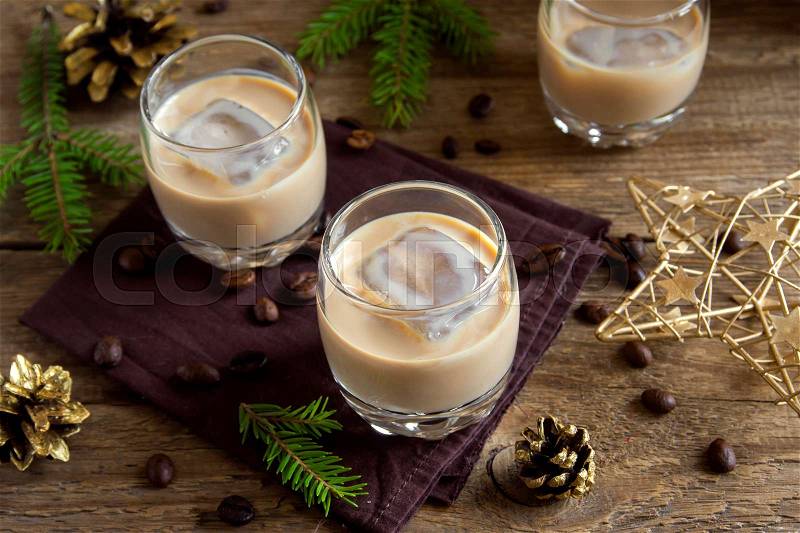 Irish cream coffee liqueur with ice, Christmas decoration and ornaments over rustic wooden background - homemade festive Christmas alcoholic drink, stock photo